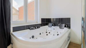 A modern bathroom with a large bathtub, a window, and black tiled walls. - Le Nid Cosy 3, Balnéo et wifi (Tourcoing)