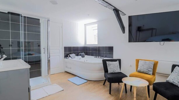 A modern room with a large bathtub, two chairs, a small table, and a TV mounted on the wall. - Le Nid Cosy 4, Balnéo 2 lits wifi (Tourcoing)