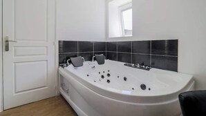 A modern bathroom with a large bathtub, black tiled walls, and a window above the tub. - Le Nid Cosy 4, Balnéo 2 lits wifi (Tourcoing)