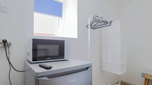 A compact kitchenette with a microwave, a small refrigerator, and a window providing natural light. - Le Nid Cosy 4, Balnéo 2 lits wifi (Tourcoing)