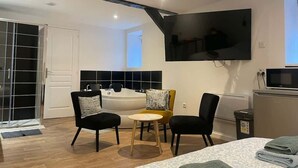 A modern room with a large bed, two armchairs, a small round table, a bathtub, and a TV mounted on the wall. - Le Nid Cosy 4, Balnéo 2 lits wifi (Tourcoing)