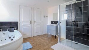 Een moderne badkamer met een ruim bad, een douche met glazen wanden en een klein wastafelmeubel.