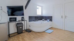 Een moderne badkamer met een bad, een wastafel met spiegel, een magnetron en een prullenbak.