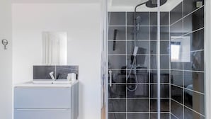 Een moderne badkamer met een douchecabine van glas, een wit wastafelmeubel met een spiegel en een klein raam.