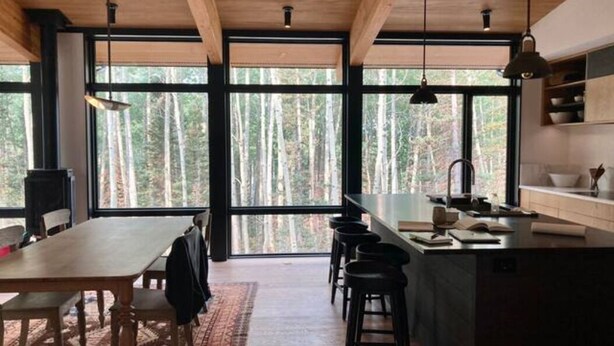 Eine moderne Küche mit einer zentralen Kochinsel, Barhocker und großen Fenstern mit Blick auf einen Wald.