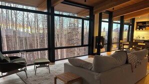 Ein geräumiges Wohnzimmer mit großen Fenstern, einem gemütlichen Sofa, einem Holztisch und einer kleinen Bank.