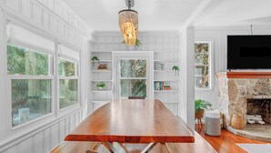 A spacious room with a large wooden dining table, white paneled walls, and a stone fireplace. - Luxury Beach Retreat Pool Walk to Beach Sleeps 12 (Melbourne Beach)