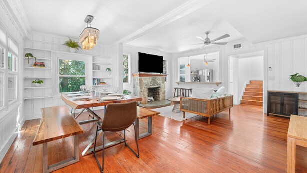 A spacious living room with a fireplace, wooden flooring, and a dining area with a bench and table. - Luxury Beach Retreat Pool Walk to Beach Sleeps 12 (Melbourne Beach)