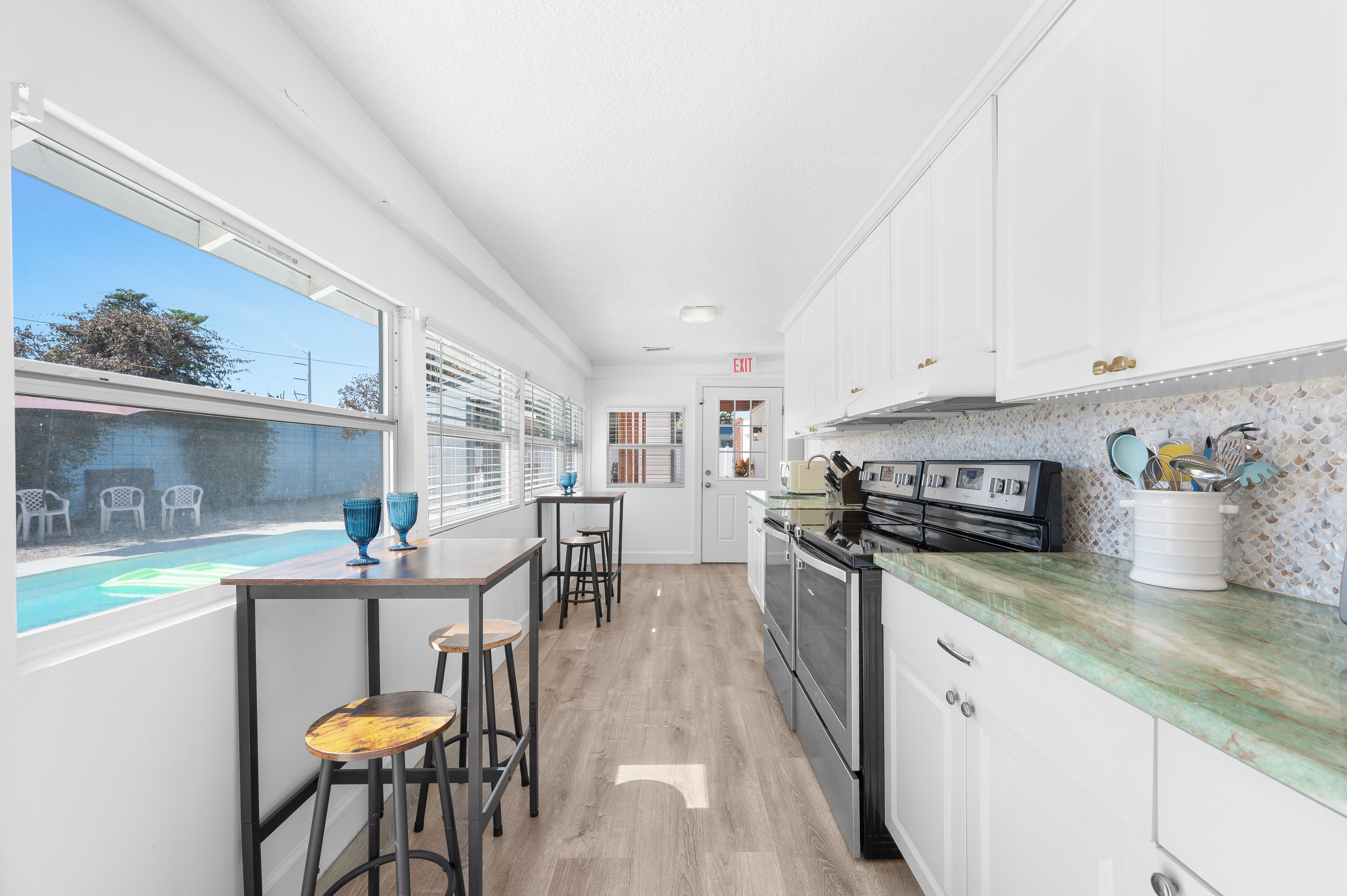 Une cuisine moderne avec des meubles blancs, un plan de travail en marbre et une vue sur une piscine.