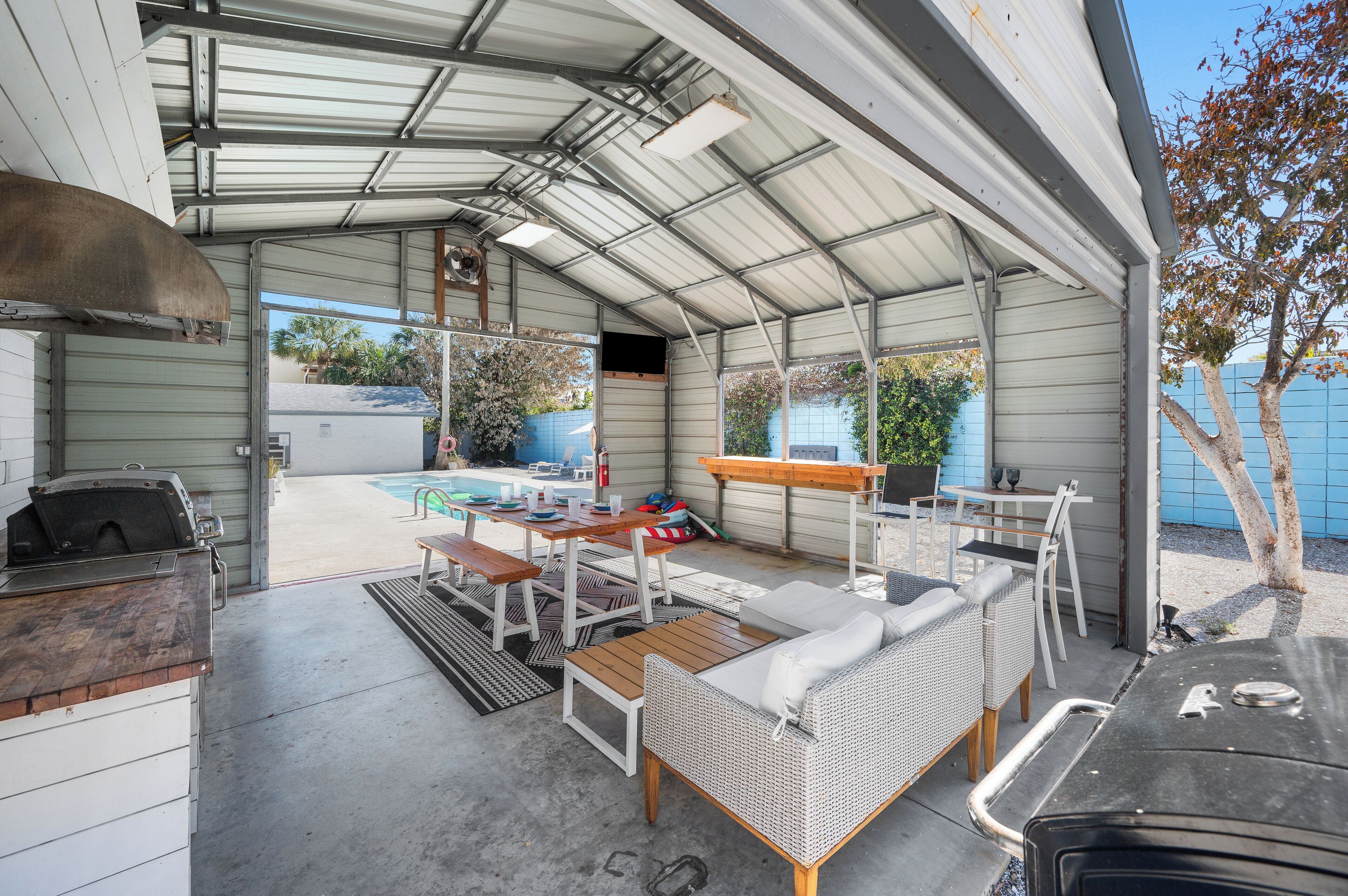 Une terrasse extérieure couverte, équipée d’un barbecue, d’un coin salon et offrant une vue sur le jardin arrière.