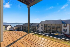 Une terrasse en bois offrant une vue sur une rangée de bâtiments et sur une étendue d’eau en arrière-plan.