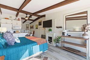 Une chambre avec un lit, une cheminée, une télévision et un coin cuisine équipé de placards et d’un four à micro-ondes.