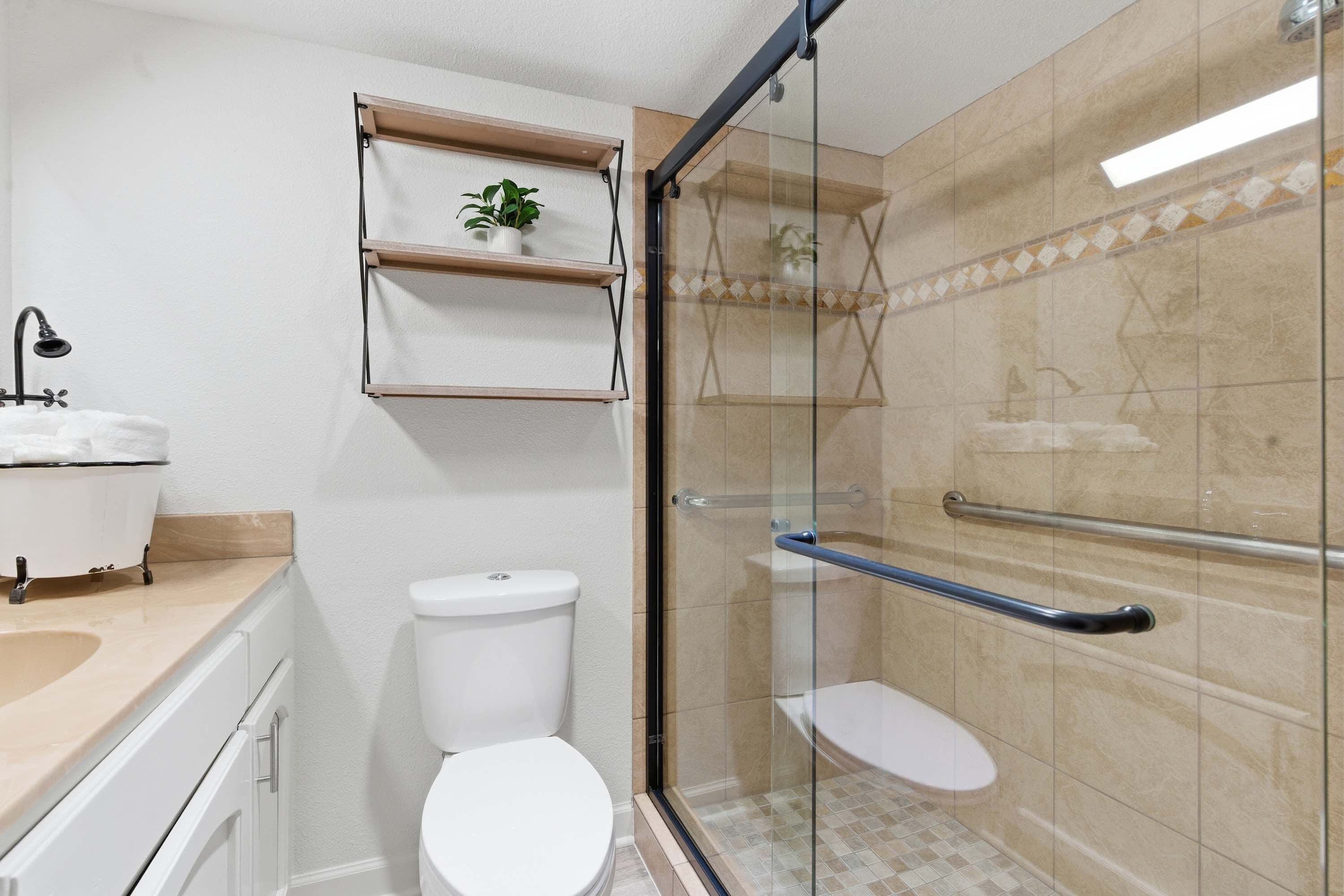 Ein modernes Badezimmer mit einer gläsernen Duschkabine, einer weißen Toilette und einem Waschbecken mit einer beigen Arbeitsplatte.