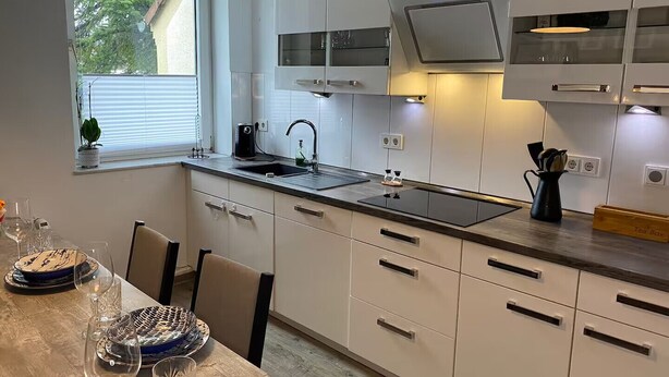 Une cuisine moderne avec des meubles blancs, un plan de travail noir et une fenêtre équipée de stores.