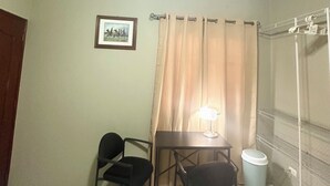 Ein Zimmer mit Deckenventilator, einem Tisch mit zwei Stühlen, einem gerahmten Bild an der Wand und einem Fenster mit Vorhängen.
