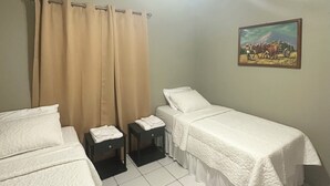 Ein Hotelzimmer mit zwei Betten, einem Deckenventilator, einem Gemälde an der Wand und einem kleinen Tisch mit einem zusammengeklappten Handtuch.