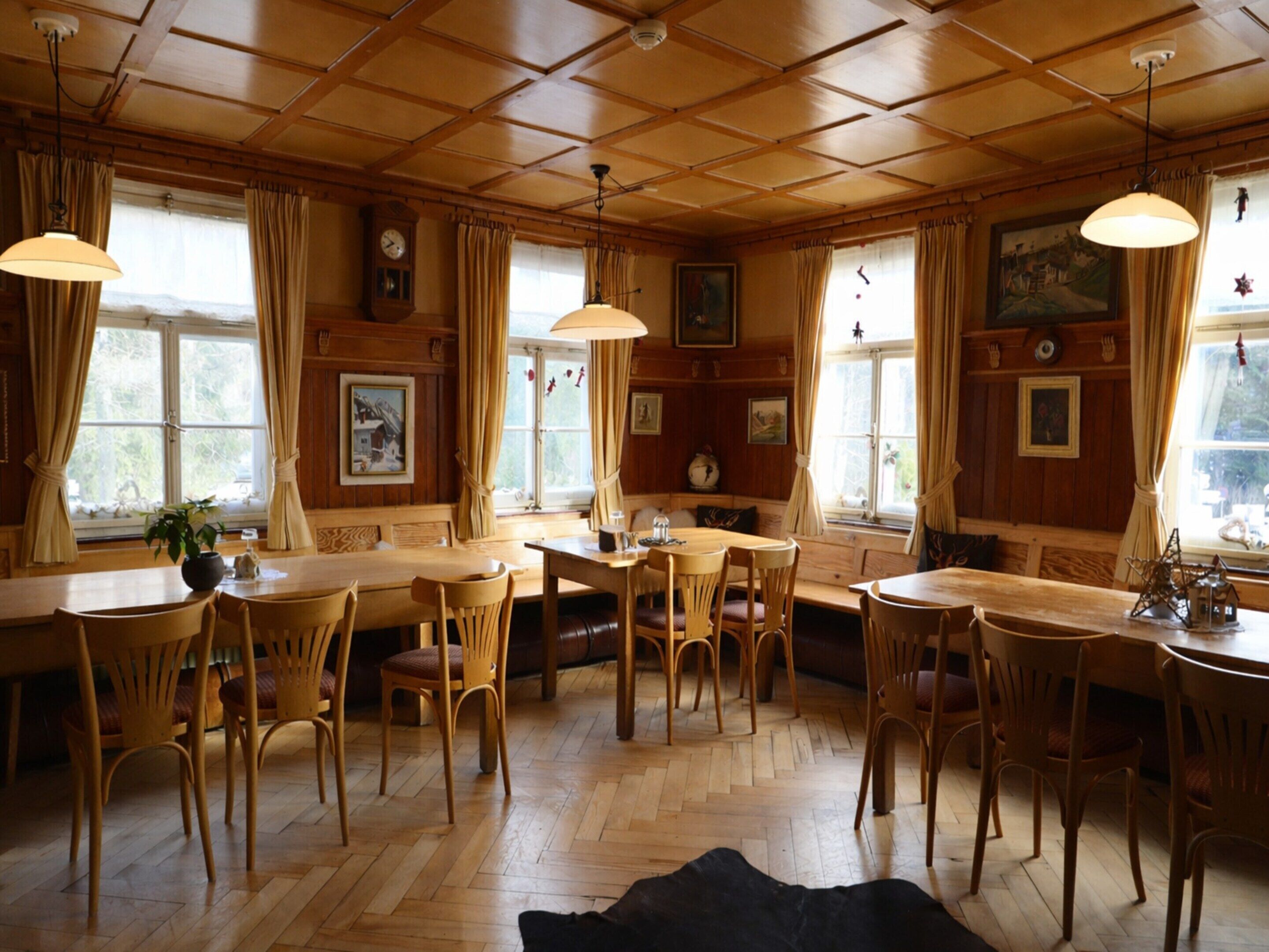 A dining area with wooden furniture, large windows with curtains, and a wooden ceiling.