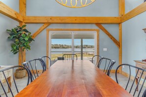 A dining area with a long wooden table and metal chairs, a potted plant, and a view through glass doors to an outdoor area. - Waterfront 4-bedroom homestead with pool, jacuzzi, and dock access. Sleeps 11! (Heathsville)