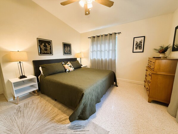 Une chambre à coucher comprenant un lit, des tables de chevet, une commode et un ventilateur de plafond.