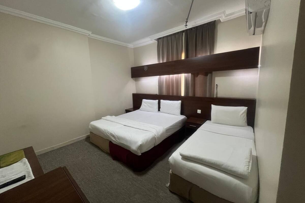 Habitación de hotel con dos camas individuales, cabecero de madera, escritorio y suelo cubierto de alfombra.