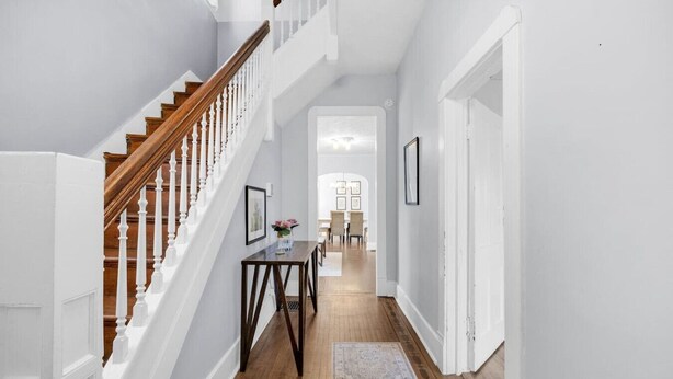 Un couloir avec un escalier en bois, un coin repas à l’arrière-plan et un tapis sur le sol.