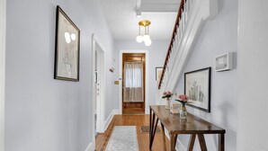 Un couloir doté d’un plancher en bois, d’un tapis, d’une table en bois ornée de vases et de tableaux encadrés accrochés aux murs.