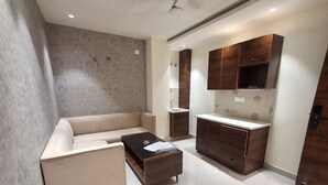 A modern living room with a beige sofa, a glass coffee table, and wooden cabinets. - IP Hill Nest By Qotel Sahastradhara (Dehradun)