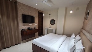 A modern hotel room with a large bed, a wooden dresser, a flat-screen TV, a round mirror, and a small bathroom area. - IP Hill Nest By Qotel Sahastradhara (Dehradun)
