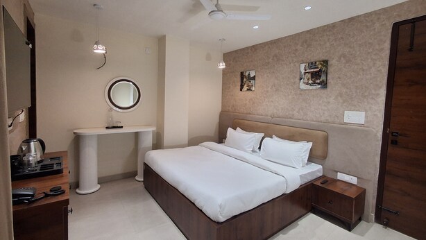 A bedroom with a bed, bedside tables, a vanity with a mirror, and a ceiling fan. - IP Hill Nest By Qotel Sahastradhara (Dehradun)