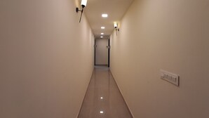 A long, narrow hallway with light-colored walls and a shiny floor. There are wall-mounted light fixtures on both sides. - IP Hill Nest By Qotel Sahastradhara (Dehradun)
