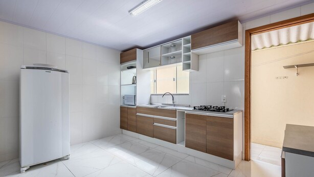 Uma cozinha moderna com armários brancos, forno embutido e pia de aço inoxidável.