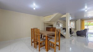 Uma sala de estar ampla com uma mesa de jantar e cadeiras, uma escada para um andar superior e um sofá em primeiro plano.