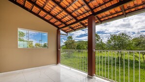 Varanda ampla com piso de azulejos, vista para uma paisagem verde e uma estrutura de pérgola.