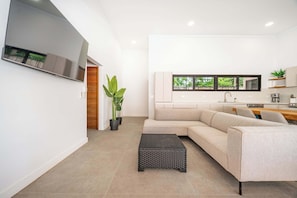 A modern living room with a sectional sofa, a flat-screen TV mounted on the wall, a small black ottoman, and a potted plant. - CASA LOLA a Modern Home in Pinilla, 3 master Bedroom and a private pool (Pinilla)