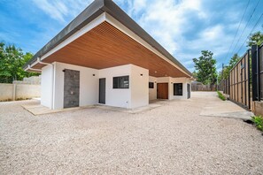 Ein modernes Haus mit überdachter Terrasse, einem Schotterweg und einem Holzzaun.