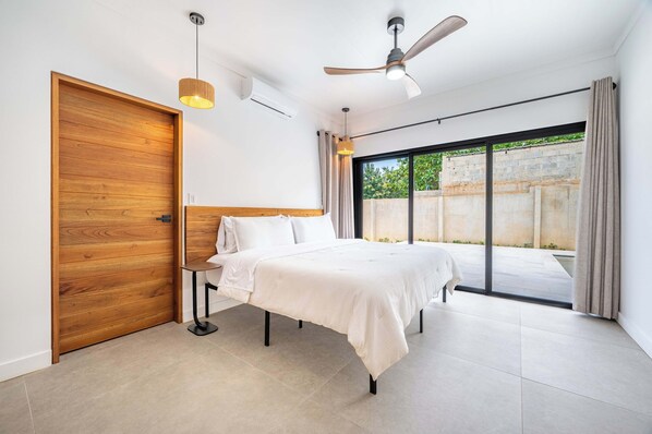 Ein modernes Schlafzimmer mit einem großen Bett, einem Deckenventilator und einer Schiebetür zu einem Balkon.