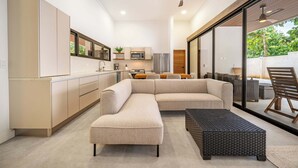 Una cocina moderna con una isla grande, un comedor con mesa y sillas, y una zona de estar con sofá y reposapiés.