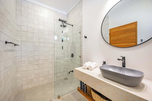 Un bany modern amb plat de dutxa tancat per vidre, un mirall gran i un lavabo de disseny.