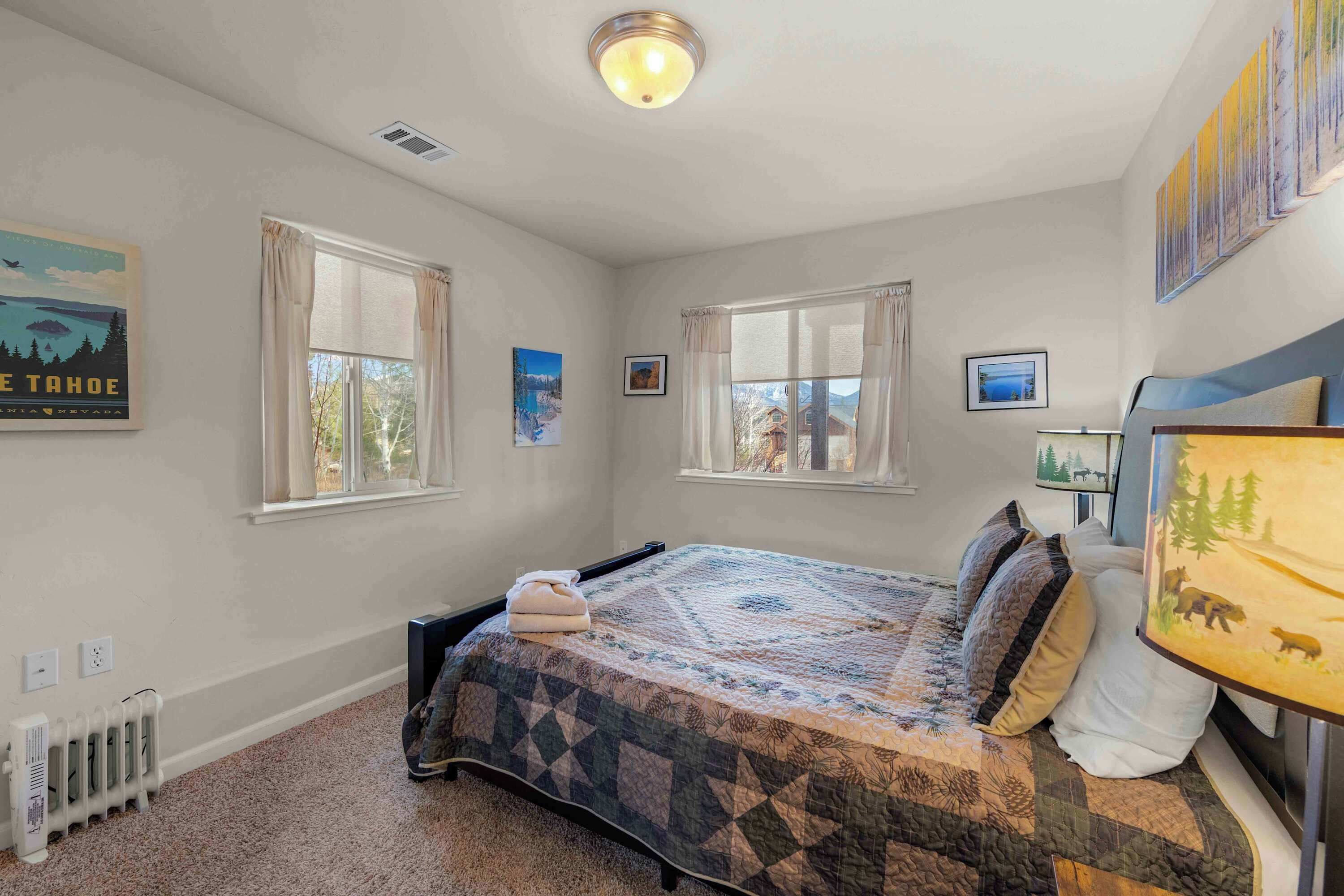 A bedroom with a bed, two windows, a radiator, and wall art.