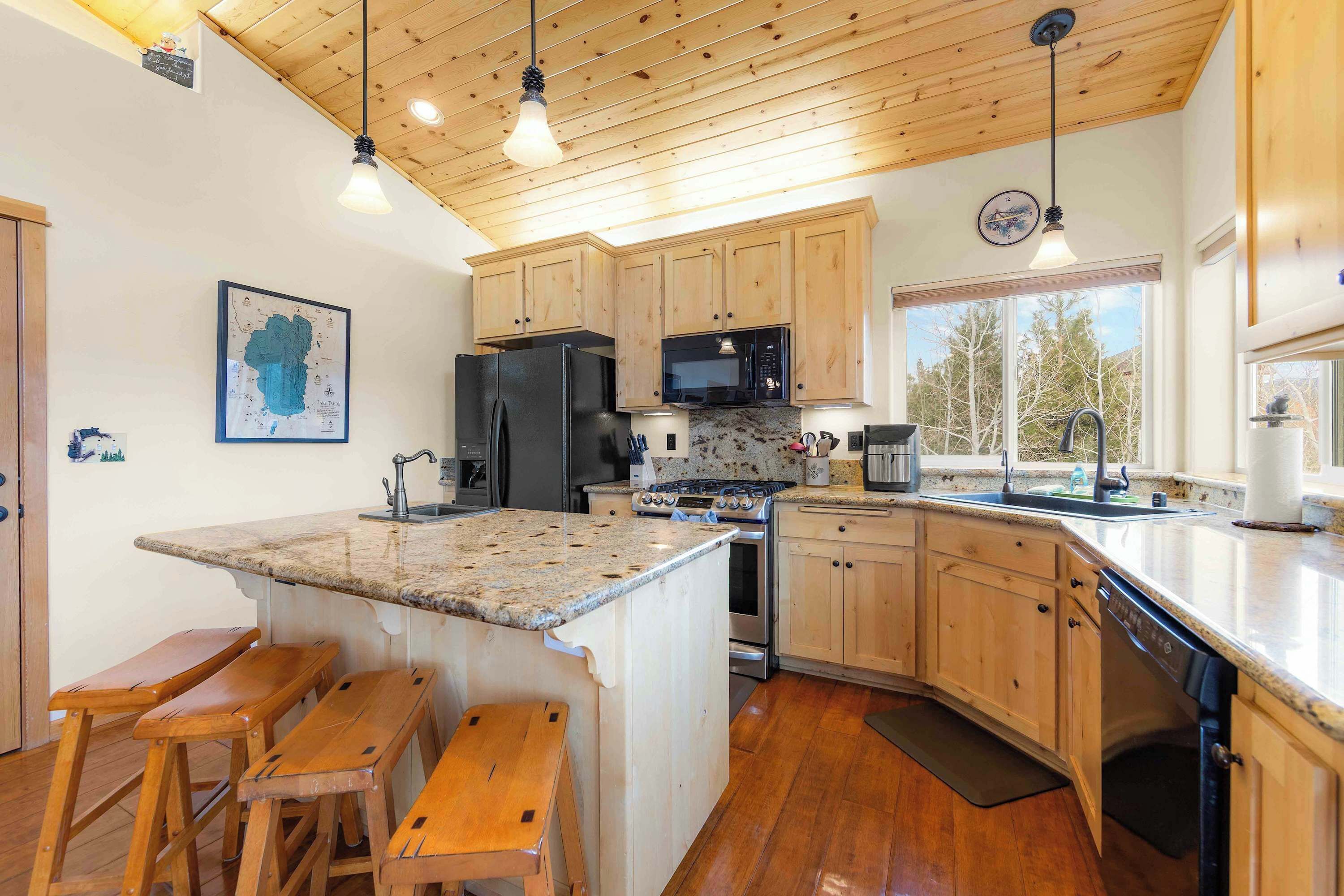 Une cuisine dotée de meubles en bois, de plans de travail en granit, d’un îlot central avec des tabourets, d’un réfrigérateur, d’une cuisinière, d’un four à micro-ondes et d’un évier.