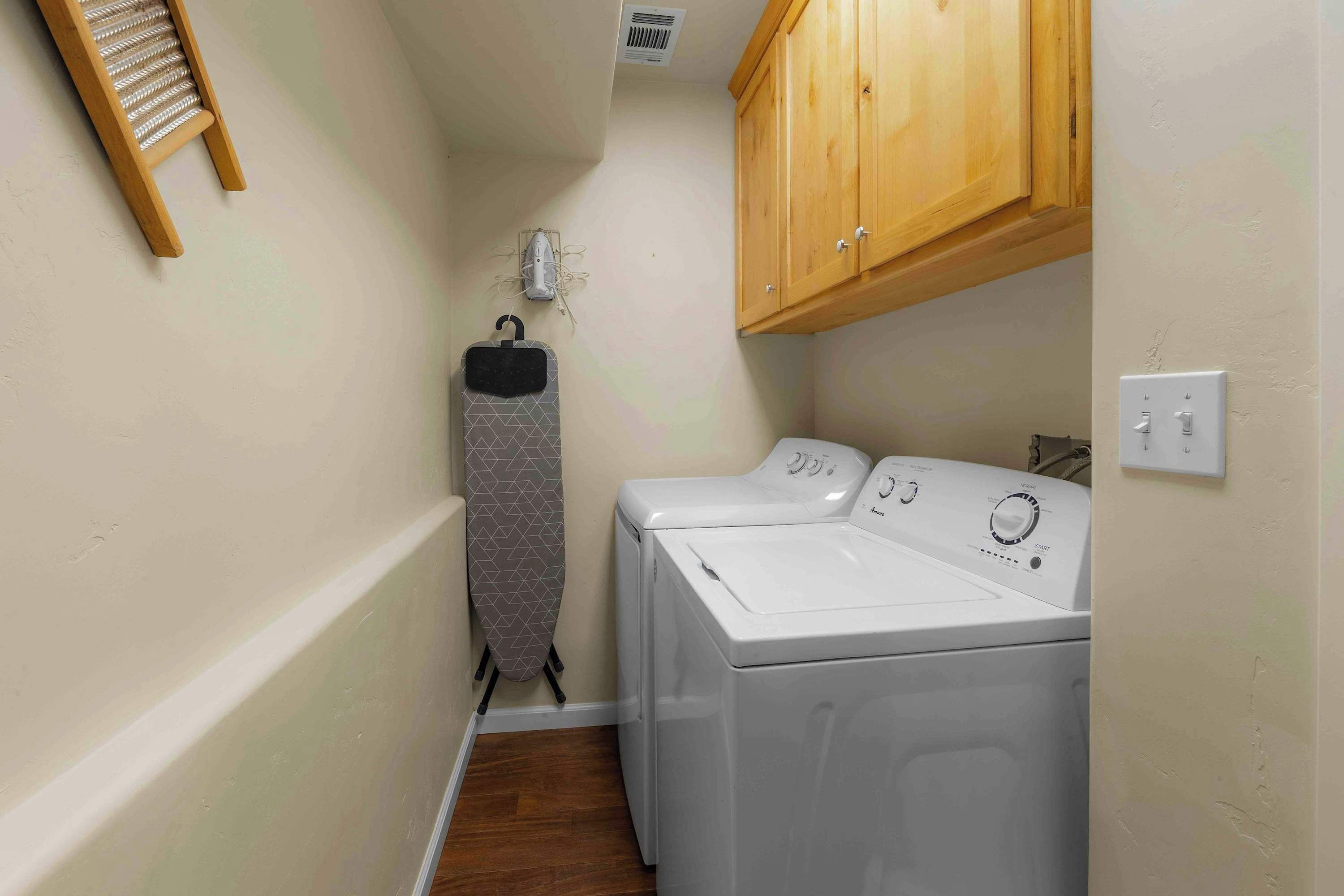 A laundry room with two white washing machines, a wooden cabinet, and a drying rack.