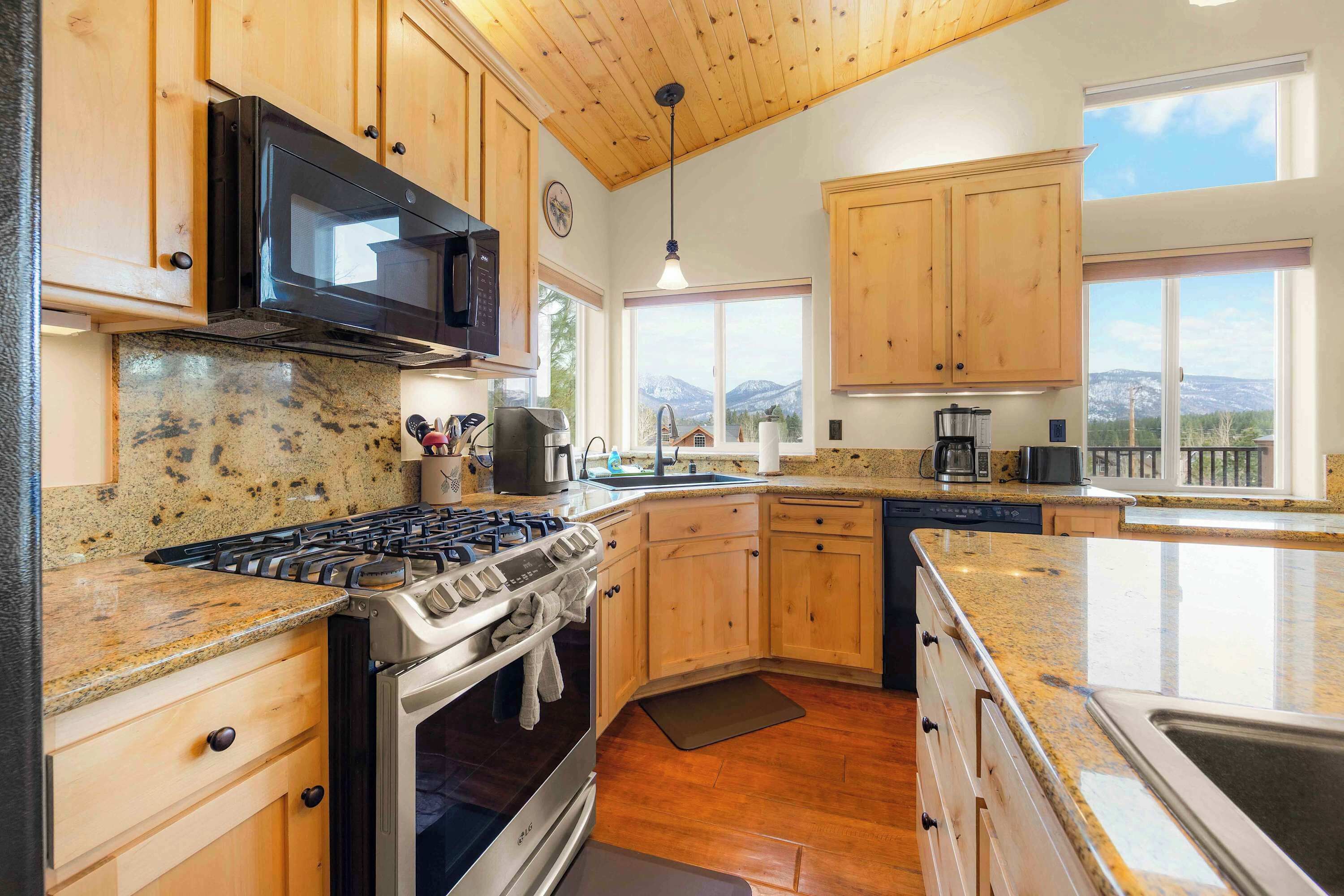 Una cocina con gabinetes de madera, encimeras de granito, estufa y microondas.