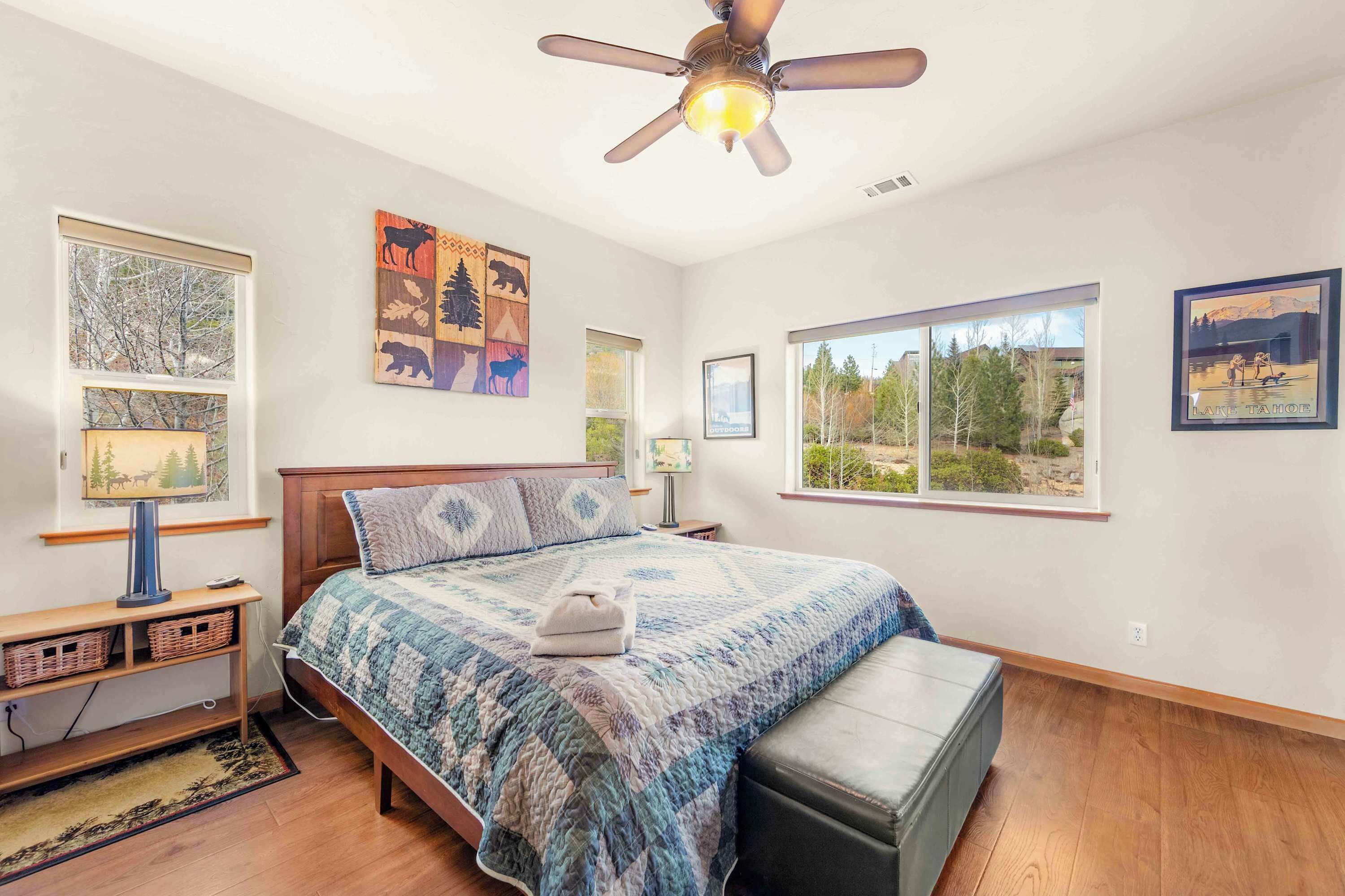 A bedroom with a bed, a ceiling fan, a window, and artwork on the walls.
