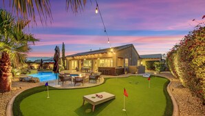 Un jardin bien aménagé avec une piscine, du mobilier de jardin et un espace dédié à l’entraînement au golf.