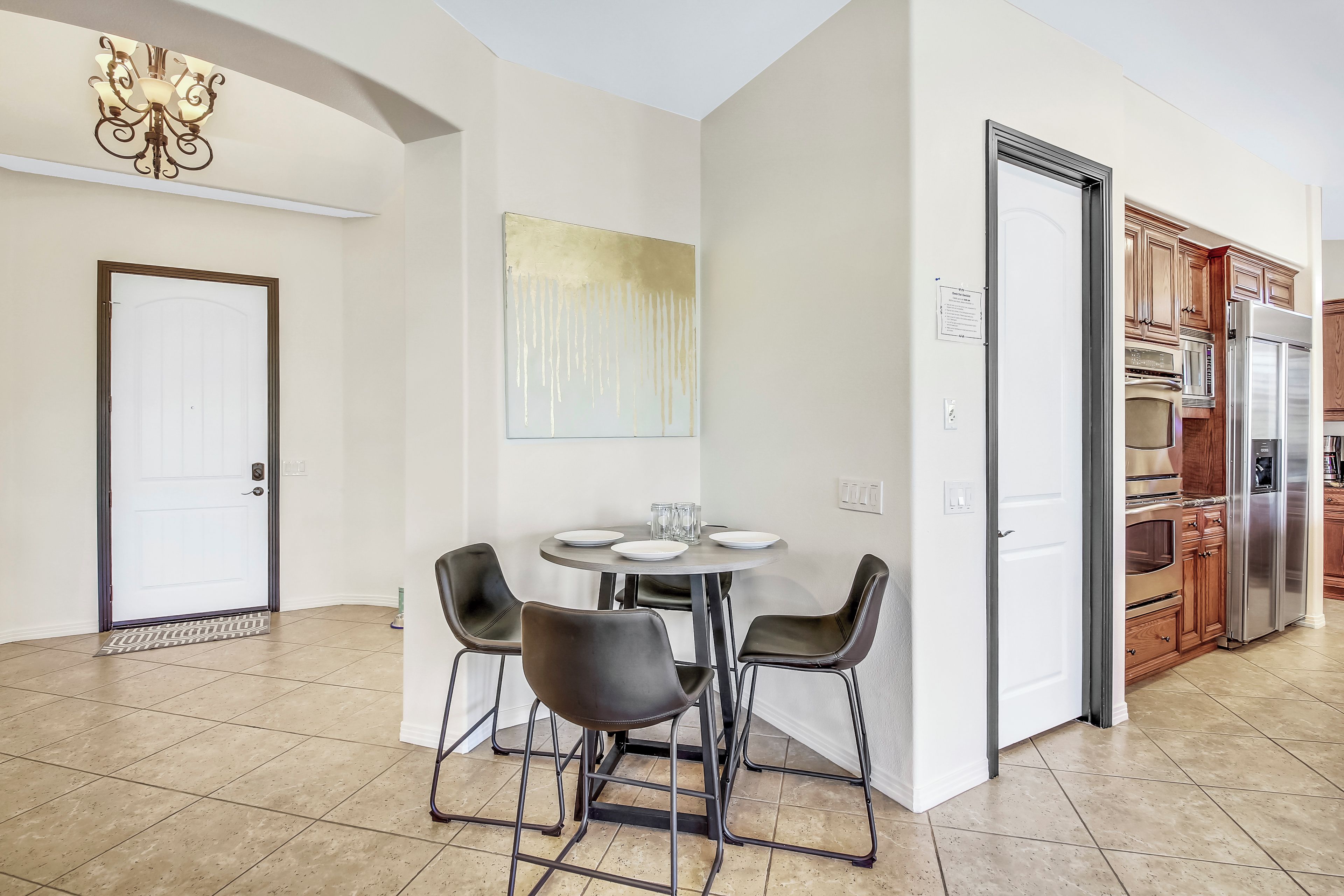 Una cocina moderna con electrodomésticos de acero inoxidable, un comedor con una mesa redonda y cuatro sillas, y una puerta blanca.