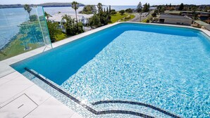 A rectangular swimming pool with clear blue water, surrounded by a tiled deck and a glass barrier.