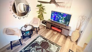 Una sala de estar con televisor, un espejo redondo, una planta y una chimenea.