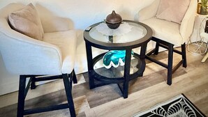 Una habitación con dos sillones, una mesita redonda con un cuenco decorativo, un espejo con diseños circulares y una planta en maceta.