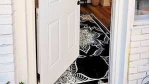 Una puerta blanca adornada con un adorno y un tapete blanco y negro que conduce al interior.
