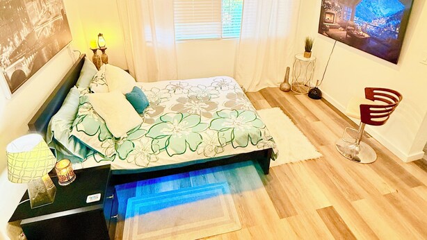 Un dormitorio con cama, televisor, lámpara y una silla.